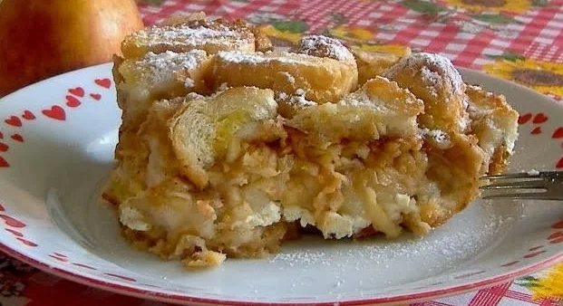 Kousek žemlovky posypaný moučkovým cukrem na talíři.