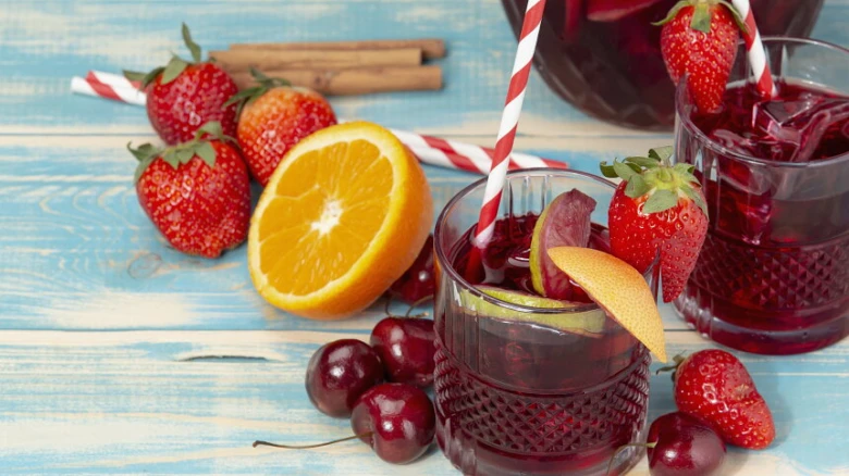 Sklenice s sangrií ozdobená ovocem na modrém dřevěném povrchu.