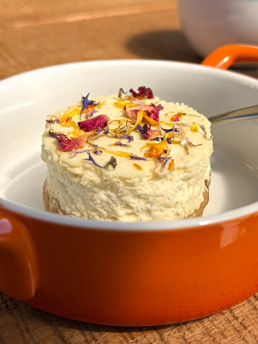 Hotový tvarohový cheesecake s květinami v oranžové misce.