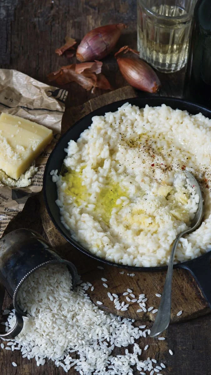Pánva s rýžovým rizotem obklopená surovými ingrediencemi.