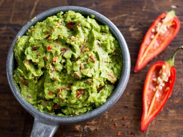 Mísa s čerstvým guakamolem vedle dvou rozkrojených červených chilli papriček.