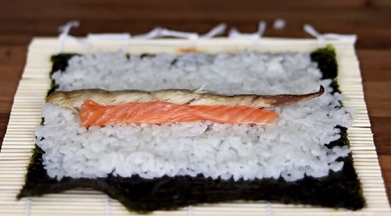 Příprava sushi s lososem na rýži před svíjením.