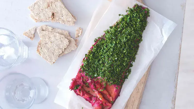 Gravlax losos s bylinkami a kousky chleba na bílé podložce.