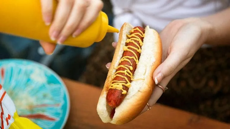 Lidé připravují domácí hotdog s hořčicí na stůl.