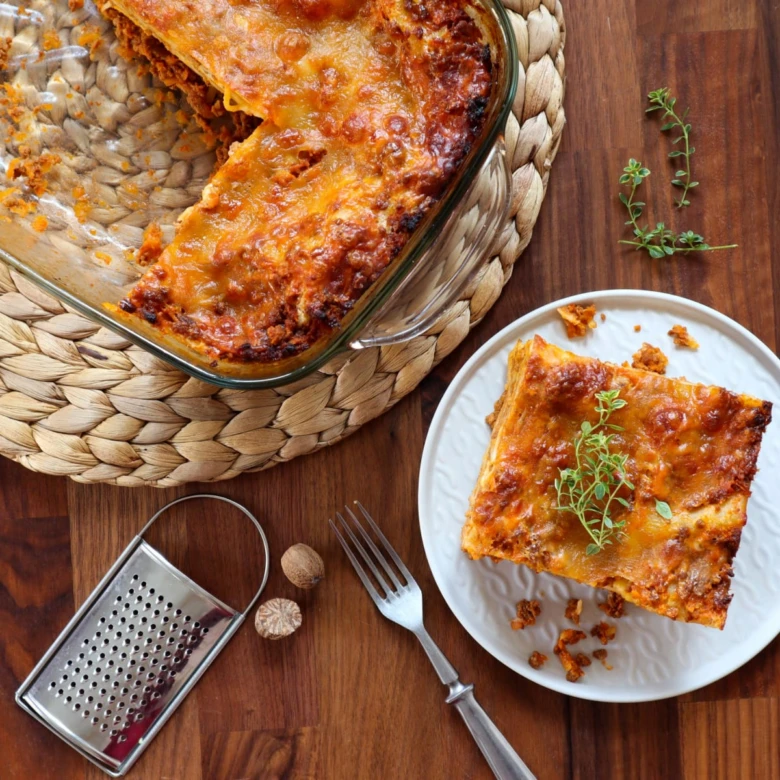 Domácí lasagne s čerstvými bylinkami na bílém talíři.