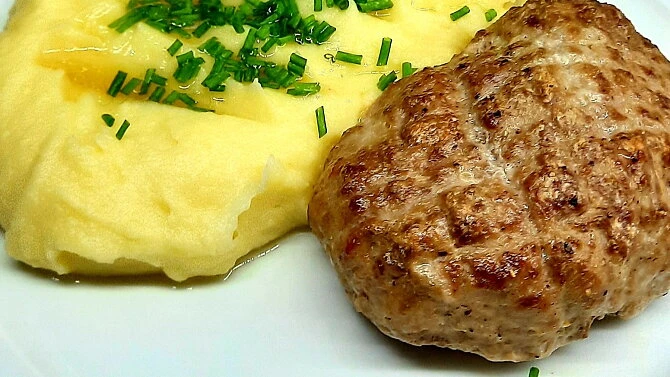 Zapečený řízek s bramborovou kaší a nasekanou česnekovkou.
