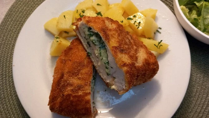 Opečený kuřecí řízek s náplní podaný se zapečenými bramborami.