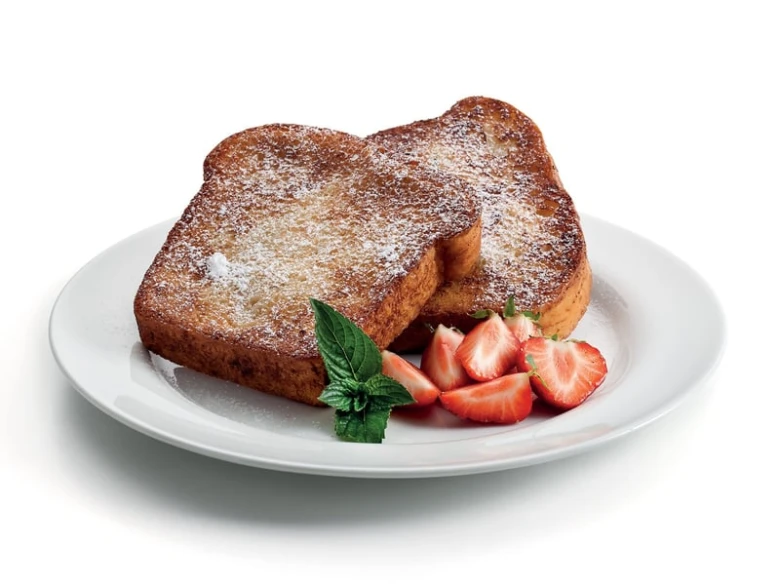 Zlatohnutý francouzský toast s jahodami na bílém talíři.
