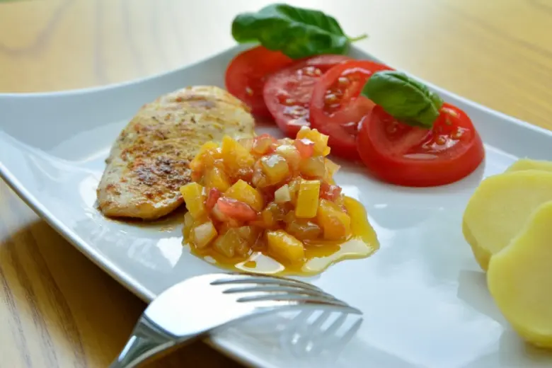 Grilovaný kuřecí steak s rajčatovou omáčkou na bílém talíři.