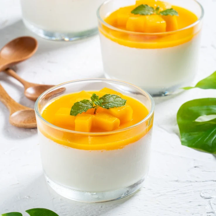 Tři skleničky s italským dezertem panna cotta s mangovým vrstvou.