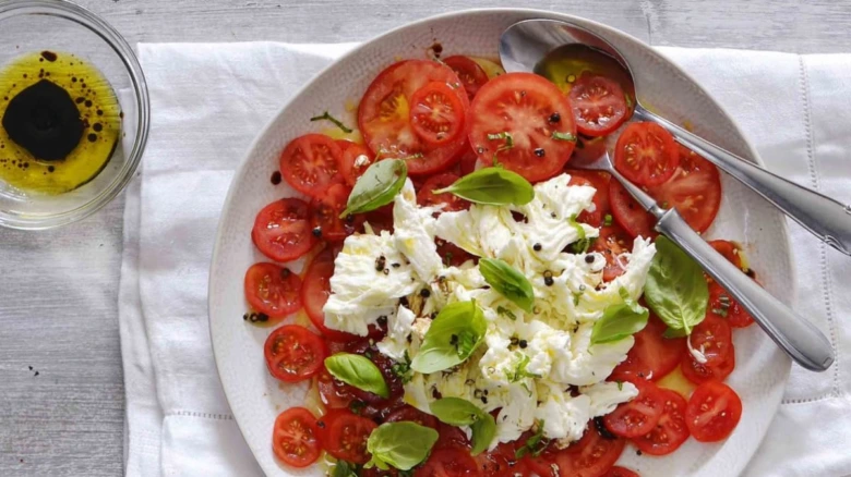 Caprese salát s rajčaty, bazalkou a mozzarellou na bílém talíři.