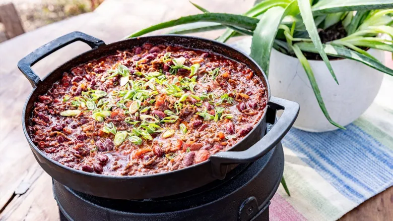Chilli con carne v hrnci s cibulkou na stolu.