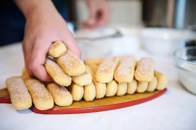 Ruce skládají žlouté piškoty na dřevěný talíř.