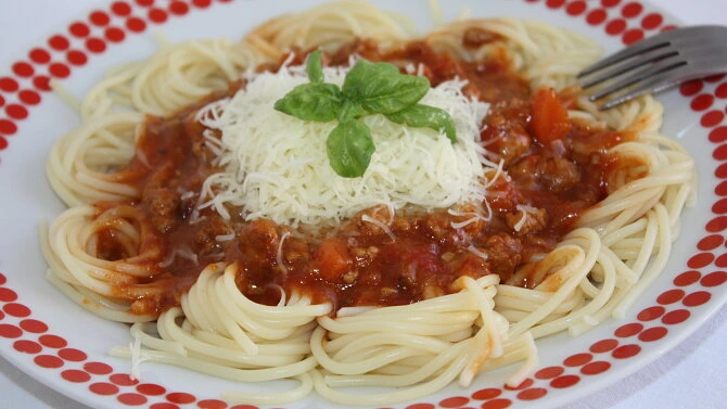 Pasta s boloňskou omáčkou, sýrem a bazalkou na talíři.