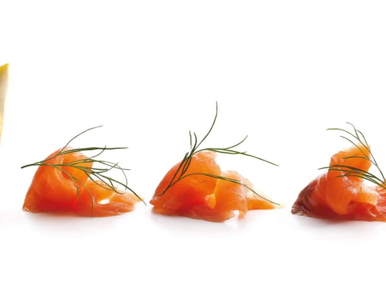 Tři kousky lososa gravlax s čerstvou koprem na bílém pozadí.