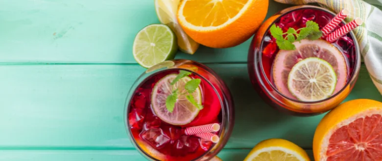 Dva sklenice s sangrií ozdobené citrusy a mátou na modrozeleném dřevěném povrchu.