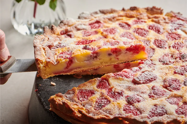 Svěží malinový koláč s krémovou náplní a cukrem na stříbrném podstavci.