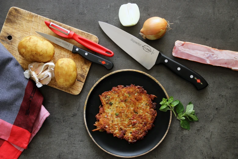 Hotové bramborové placky s surovými ingrediencemi na tmavém povrchu.