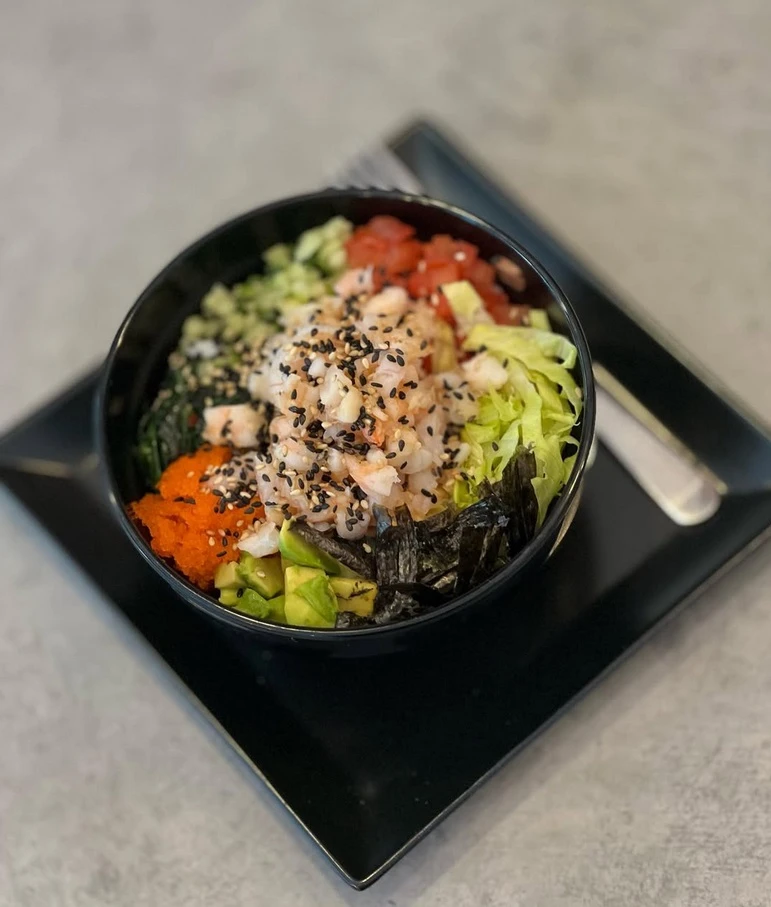 Černá miska s rýží a čerstvými ingrediencemi pro poke bowl.