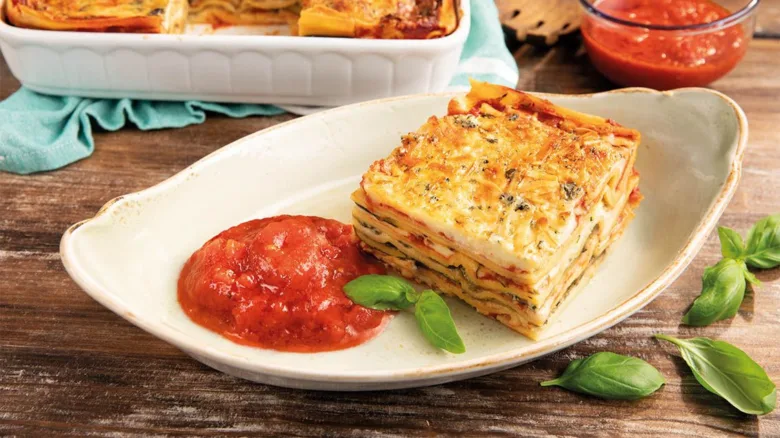 Kousek zeleninového lasagne s rajčatovou omáčkou na talíři.