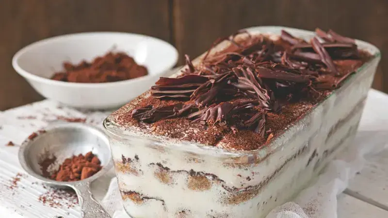 Tiramisu s čokoládovými strouhankami a kakaem v skleněné mise.