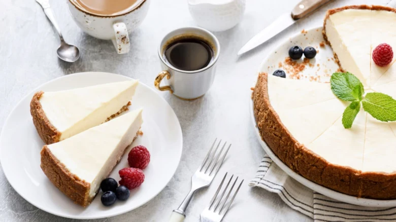 Pečený cheesecake s ovocem na bílém podkladu vedle kávy.