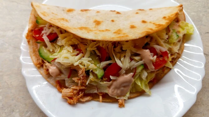 Hotová tacos s trhaným kuřecím masem na bílém talíři.