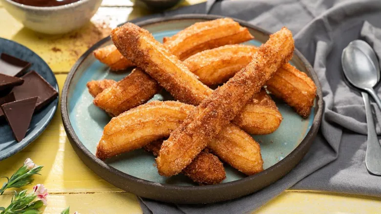 Zlatohnědé churro s cukrem a čokoládou na talíři.