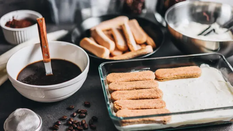 Příprava tiramisu s piškoty, kávovou omáčkou a smetanovým krémem.