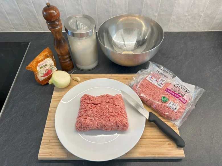 Surová hovězí mleté maso s cibulí a kořením pro domácí burgery.