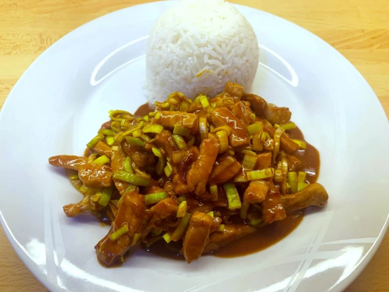 Pekingská omáčka s masem a rýží na bílém talíři.