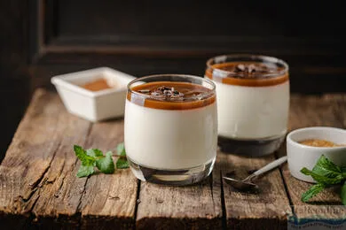 Tři skleničky s italským dezertem panna cotta na dřevěném stole.