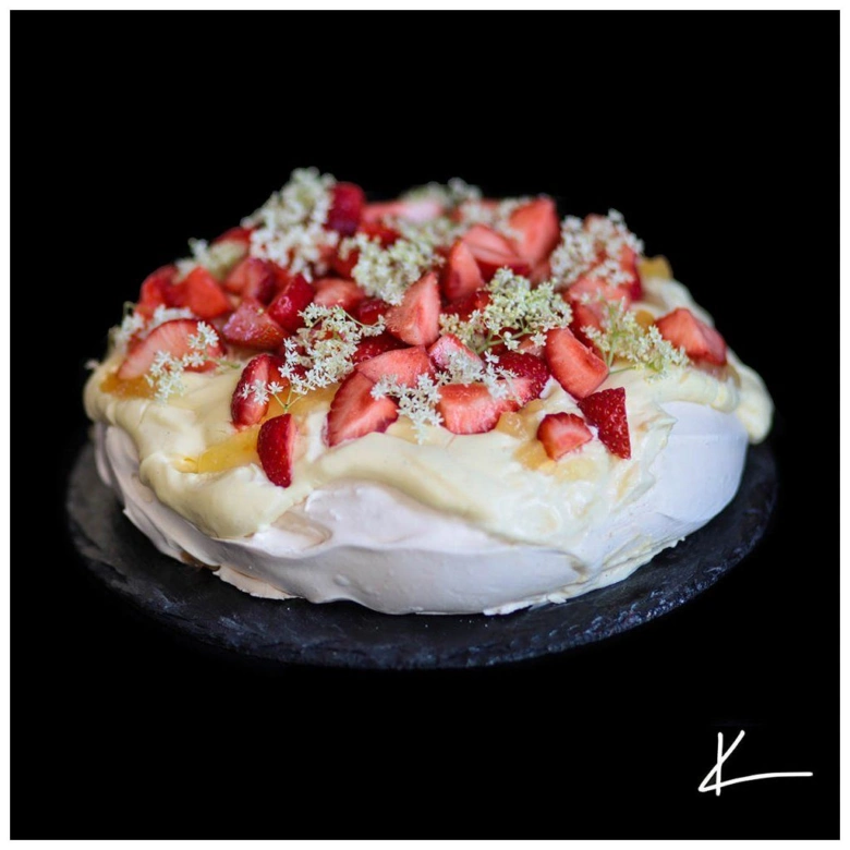 Celý dezert pavlova s jahodami na tmavém podstavci.