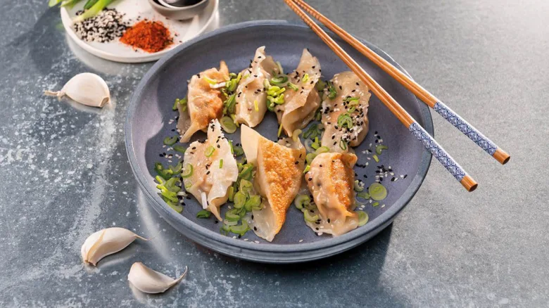 Pálené japonské gyoza knedlíčky s cibulkou a sezamem na talíři.