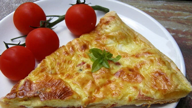 Kus slaného koláče s bazalkou a rajčaty na talíři.