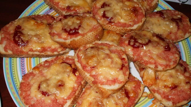 Zapečené tousty sýrovou omáčkou a ovocným džemem na talíři.