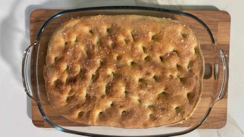 Svěžě upečená focaccia v skleněné míse na dřevěném prknu.