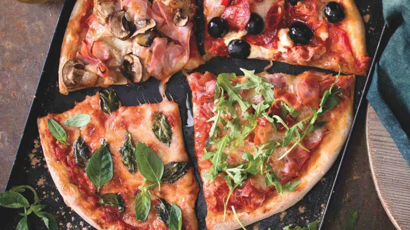 Pizzu s různými ingrediencemi na tmavém podnosu.