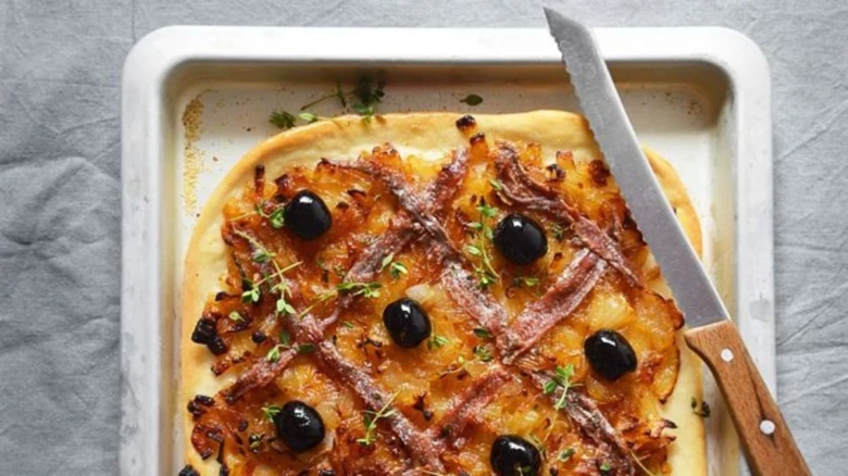 Pizza s ančovičkami, černými olivami a bylinkami na plechu.