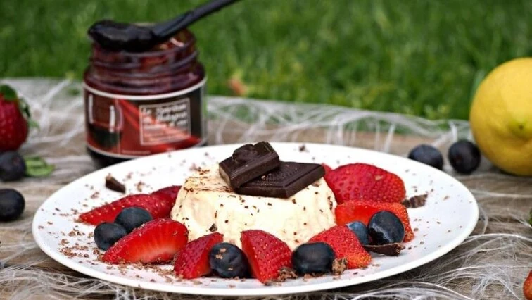 Panna cotta s ovocem a čokoládou na bílém talíři venku.