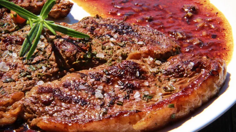 Pekně opečený steak s bylinkami a červenou omáčkou na talíři.