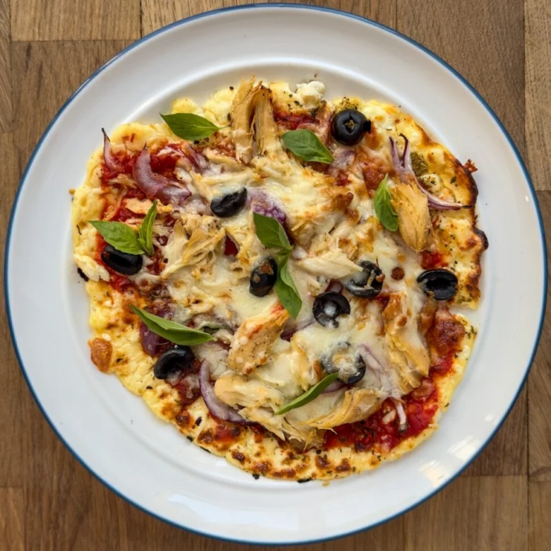 Hotová cottage pizza s kuřetem, olivami a bazalkou na talíři.