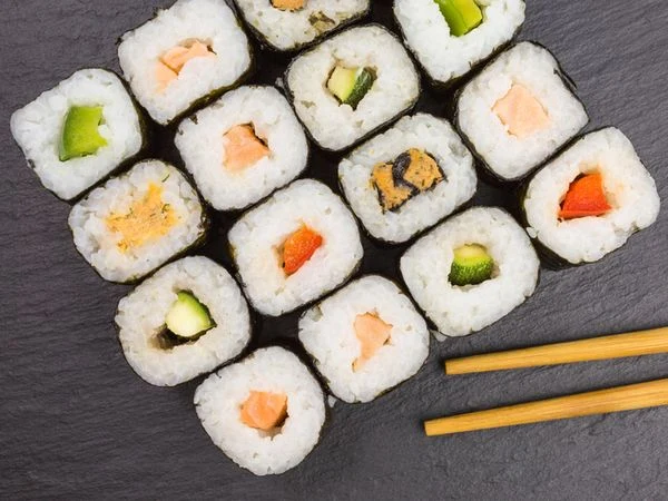 Různé druhy sushí na tmavém podkladu vedle hřídel.