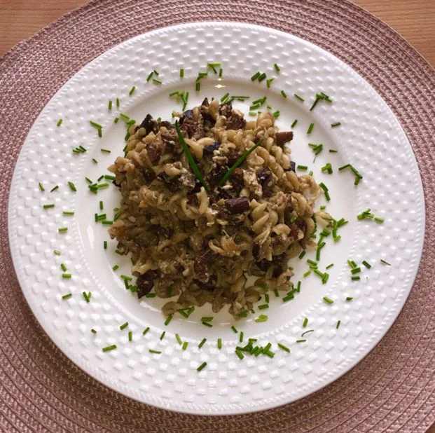 Pasta s houbami na bílém talíři posypaná nasekanou bylinkou.