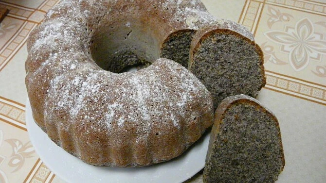 Maková bábovka nakrájená na talíři s posypem moučkovým cukrem.