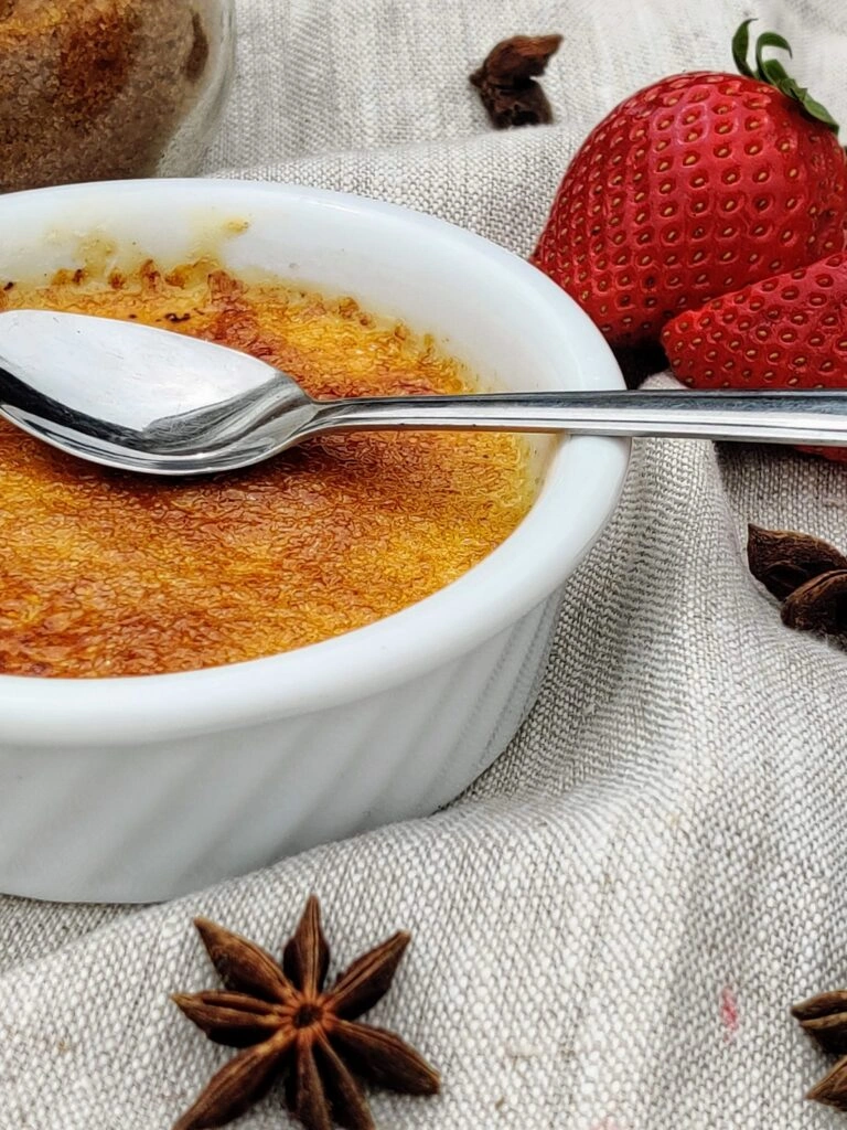 Klasická crème brûlée s karamelem v bílé misce vedle jahod.