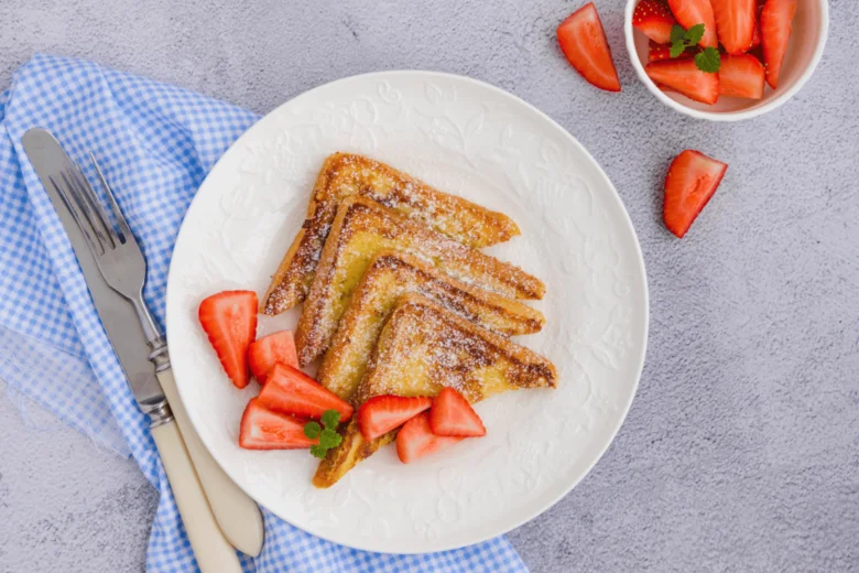 Zlatý francouzský toast s jahodami na bílém talíři.