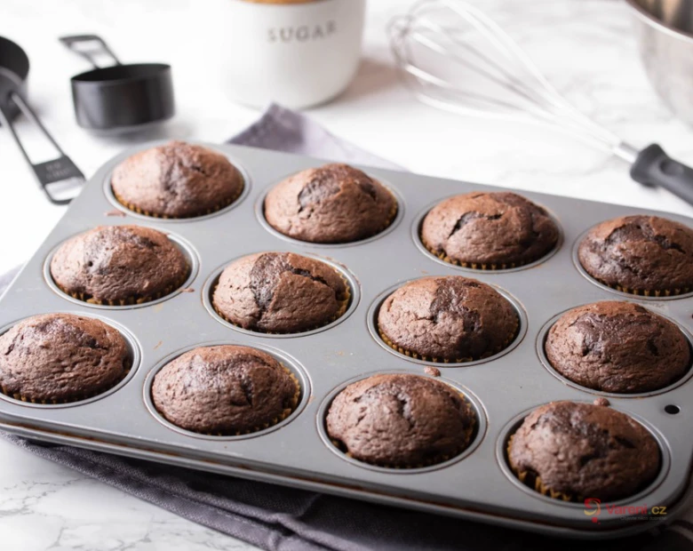 Čerstvě upečené čokoládové muffiny v plechu na mramorovém povrchu.