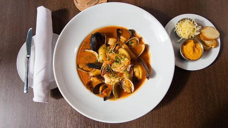 Bílá mísa s rybí polévkou se mušlemi a krevetkami.