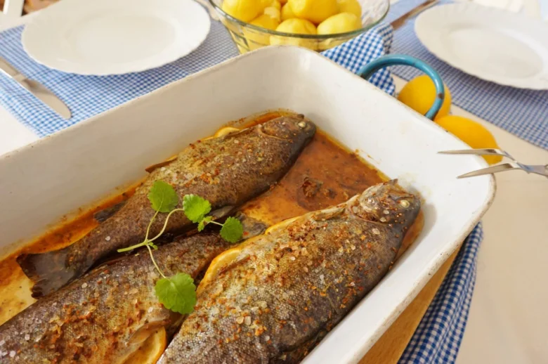 Dva pečené pstruhy v bílé mýdlovce s citronem na stolu.